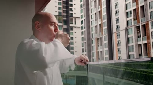 Bald Man Drinking on Balcony Overlooking City