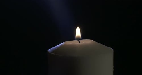 Slow motion close up footage of a white candle on a dark background