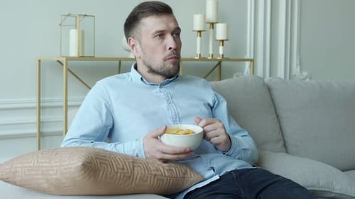 Man Sits on the Couch and Eats Potato Chips