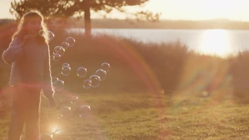 Little Girl Blowing Bubbles In Countryside At Sunset