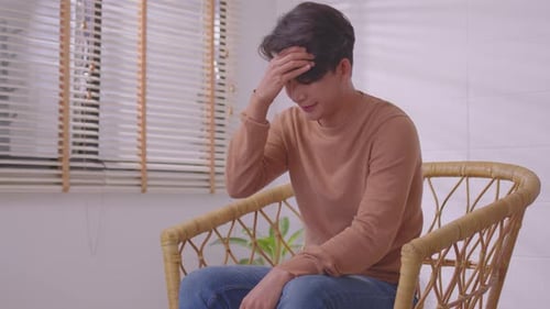 Young Man with Headache Sitting in Wicker Chair