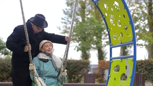 Senior couple on a playground, swinging on the swing set.