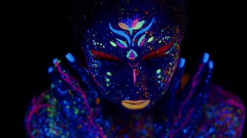Woman with body art made with luminous fluorescent paints, open eyes and looks into camera
