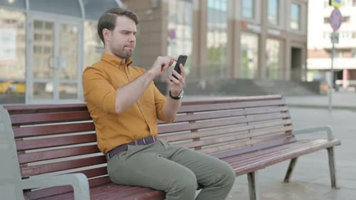 Man Using Phone on Bench in Urban Setting