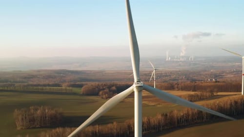 Close Up a Large Spinning Wind Turbine on the Background of Wind Farm at Sunset