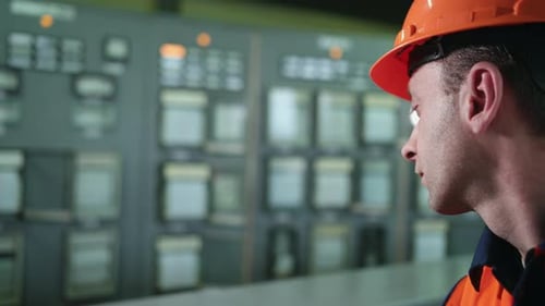 Engineer in Orange Safety Vest Inspects Control Panel