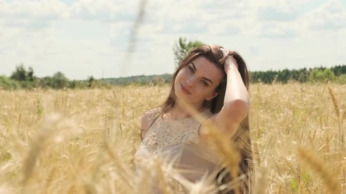 Beautiful Sexy Woman in Field of Rye or Wheat Playfully Looks at Camera and Straightens Her Hair
