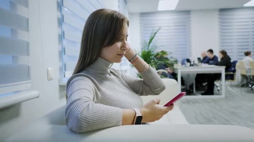 Closeup of a Modern Girl Uses a Mobile Phone on the Couch in the Office Scrolls Types Text Surfs the