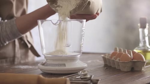 The flour in paper bag falls in transparent measuring bowl. Mechanical kitchen scale for measuring