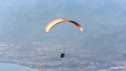 Gleitschirmflieger fliegen mit Gleitschirmfliegen im Himmel über Wald, Berggipfel und Meer