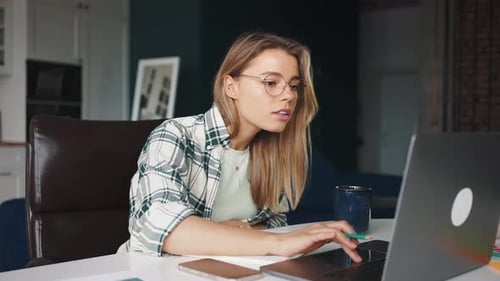 Woman Working at Laptop and Writing in Notebook
