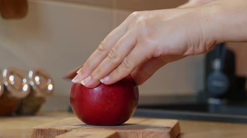 Frau schneidet einen reifen roten Apfel mit einem Messer.