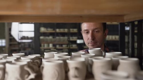 Potter Inspects Ceramic Mug on Workshop Shelf