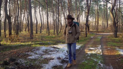 Backpacker with Camera Walks Along a Trail in the Forest