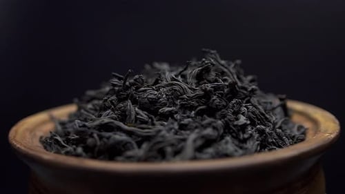 Close Up View Dry Black Tea Leaves Rotate in a Clay Bowl on Black Background