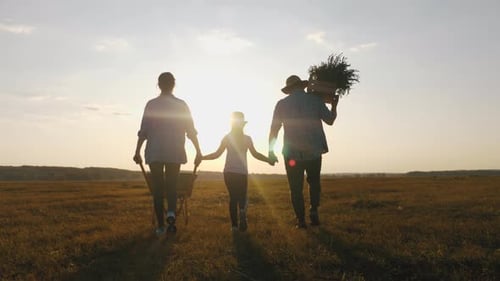 Young Family Having Fun Outdoors in Their Farm, Gardener Woman Pushing Wheelbarrow with Vegetables