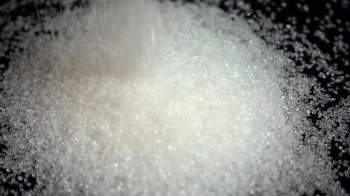 Falling grains of sugar on a black mirror background. Slow motion.