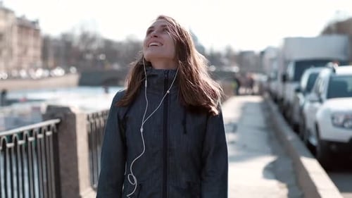 Emotional Girl Walks in City Along the River She Listen Music in Headphones