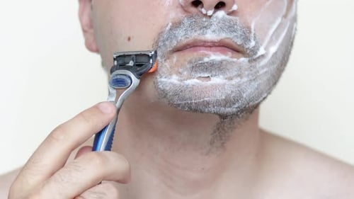 jovem com espuma de barbear no rosto está sorrindo.cara usando navalha para raspar a barba.sentindo dor.diariamente