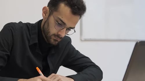 Man Writing at Desk With Laptop