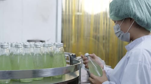 Superviseur féminin asiatique inspectant une chaîne de production de bouteilles de boissons aux herbes