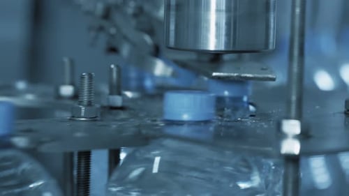 Close-up: Automatic Machine Tighting the Plastic Cap on Plastic Bottle