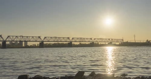 Timelapse of City River Bank. Sun Rays, Blue Sky and Railway Bridge Over Horizont. Summer Sunset