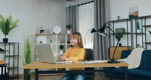 Chica con auriculares sentada frente al portátil y hablando con el profesor durante la videoconferencia