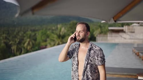 Man Talking on Phone at Tropical Resort Pool