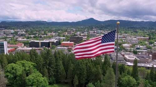 American Flag Waving Over Green Cityscape, Aerial Shot