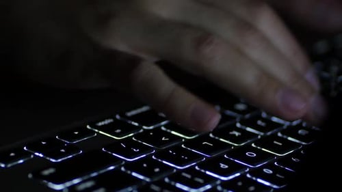 Hands Typing on Glowing Keyboard in Dark