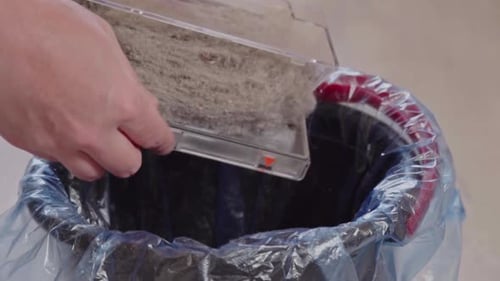 Hand Empties Dust Container into a Trash Can