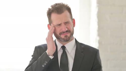Man in Suit Massaging Temples in Bright Room