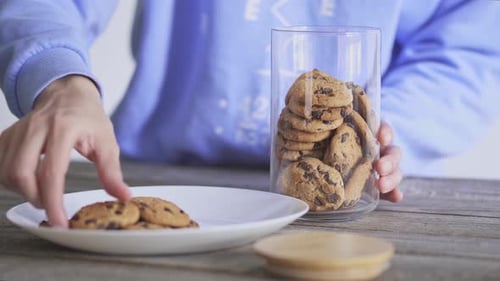 Person Placing Cookies in Glass Jar