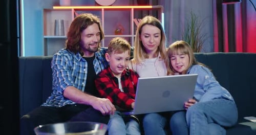 Familia descansando junta en el suave sofá por la noche y viendo cómo el niño usa la computadora portátil