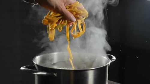 Hand Holds Pasta Over Pot of Boiling Water