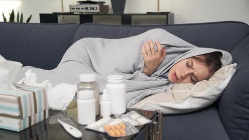Jeune femme malade avec de la fièvre allongée sur un canapé enveloppée dans un plaid et présentant des symptômes de grippe