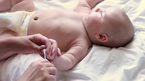 Adult Trimming Baby Fingernails on White Bed