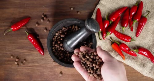Male Hand Puts Black Pepper in a Mortar with Pestle.