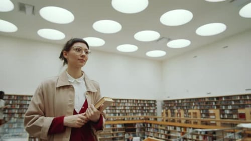 Mulher segurando um livro e andando na biblioteca