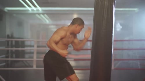 Shirtless Boxer Punching Heavy Bag in Gym