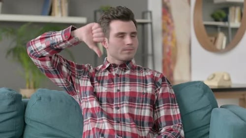 Portrait of Man Showing Thumbs Down While Sitting on Sofa