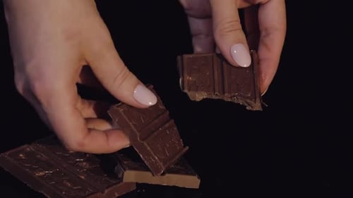 Woman Breaks Black Chocolate Bar with Nuts