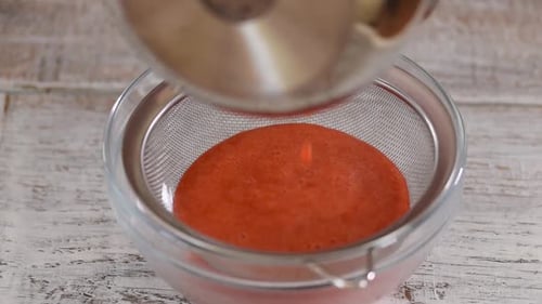 Las manos de cocinero profesional preparan puré de bayas de fresa frotando a través de un colador.