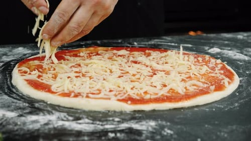 Las manos están rociando queso rallado fresco sobre la masa de pizza