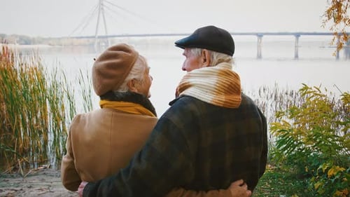 Loving Aged Pair Grandparents are Hugging Talking and Smiling While Standing on Bank of a River on