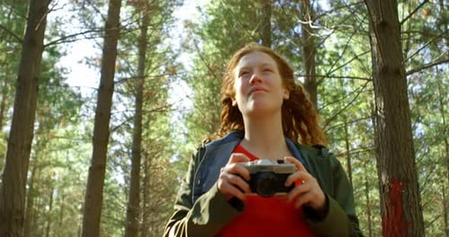 Woman Holding Camera in Sunny Forest