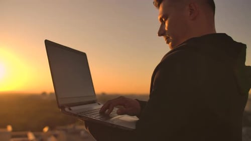 Close-up: a Programmer's Hand Typing on a Laptop Keyboard at Sunset Overlooking the Roof. A