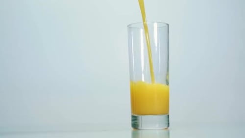 Fresh Orange Juice Pouring Into clean transparent Glass on gray table on white background . Close up