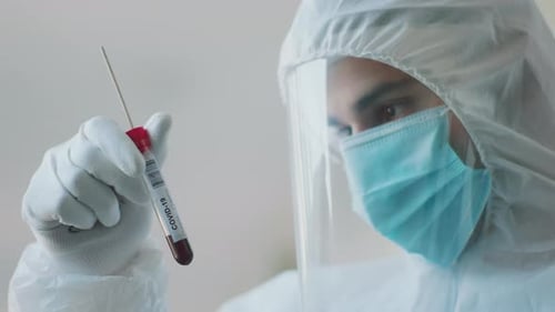 Hombre en traje de material peligroso mirando un tubo de ensayo
